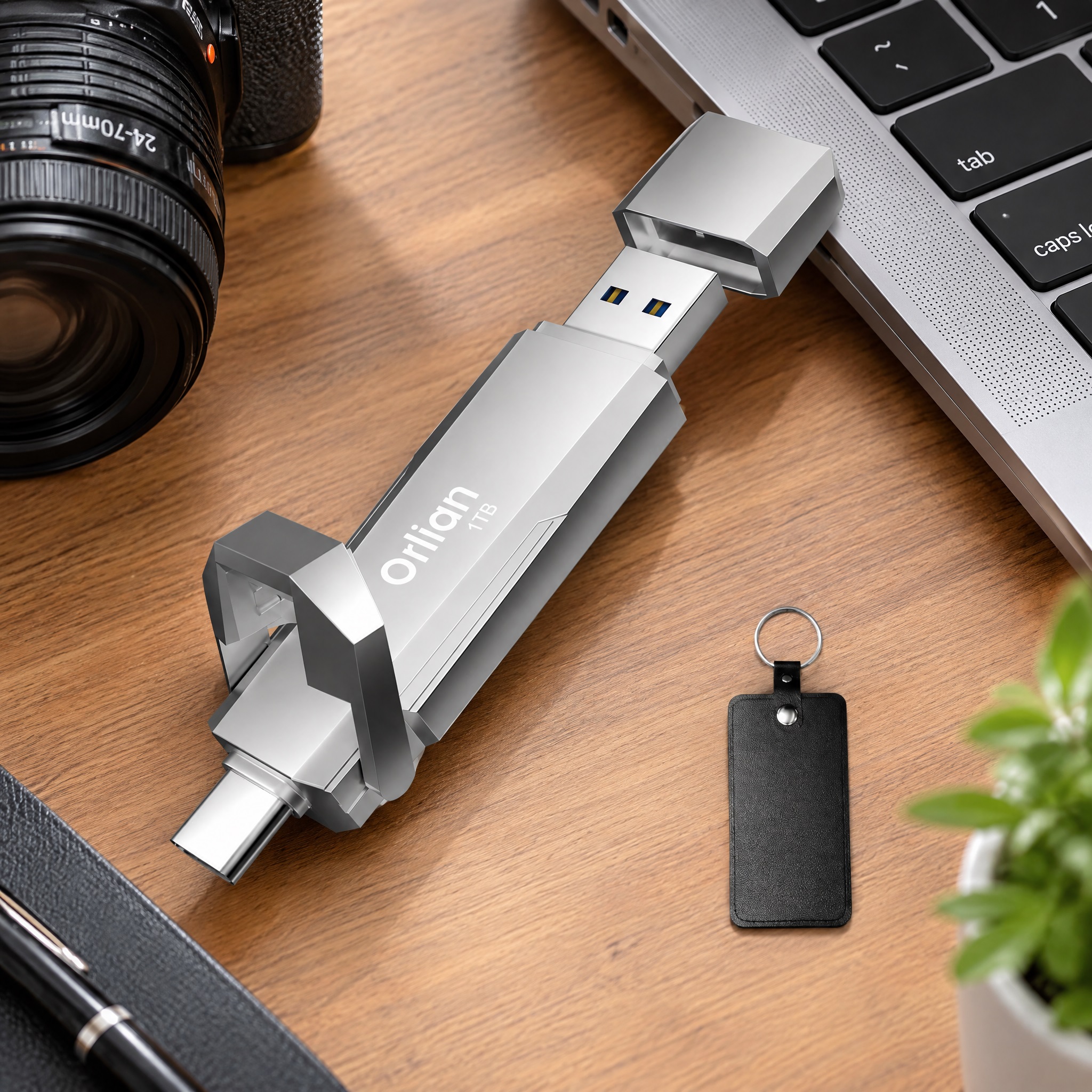 Orlian silver 1TB dual-interface portable SSD/USB drive on a wooden desk alongside a laptop, camera lens, keychain, and plant, presenting a professional modern workspace.