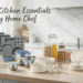 A bright Scandinavian kitchen counter showcasing Pyrex products โ glass storage containers, metal bakeware, stainless mixing bowls, ceramic bakeware, glass canisters, and ceramic cookware โ with English headline "Pyrex: Kitchen Essentials for Every Home Chef" and cartoon annotation bubbles.