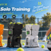 TENNIIX smart tennis ball machines in orange, black, and white on an outdoor court with a female player. Promotional graphics highlight smart solo training, flexible practice schedules, app and voice control, and wrist remote operation.
