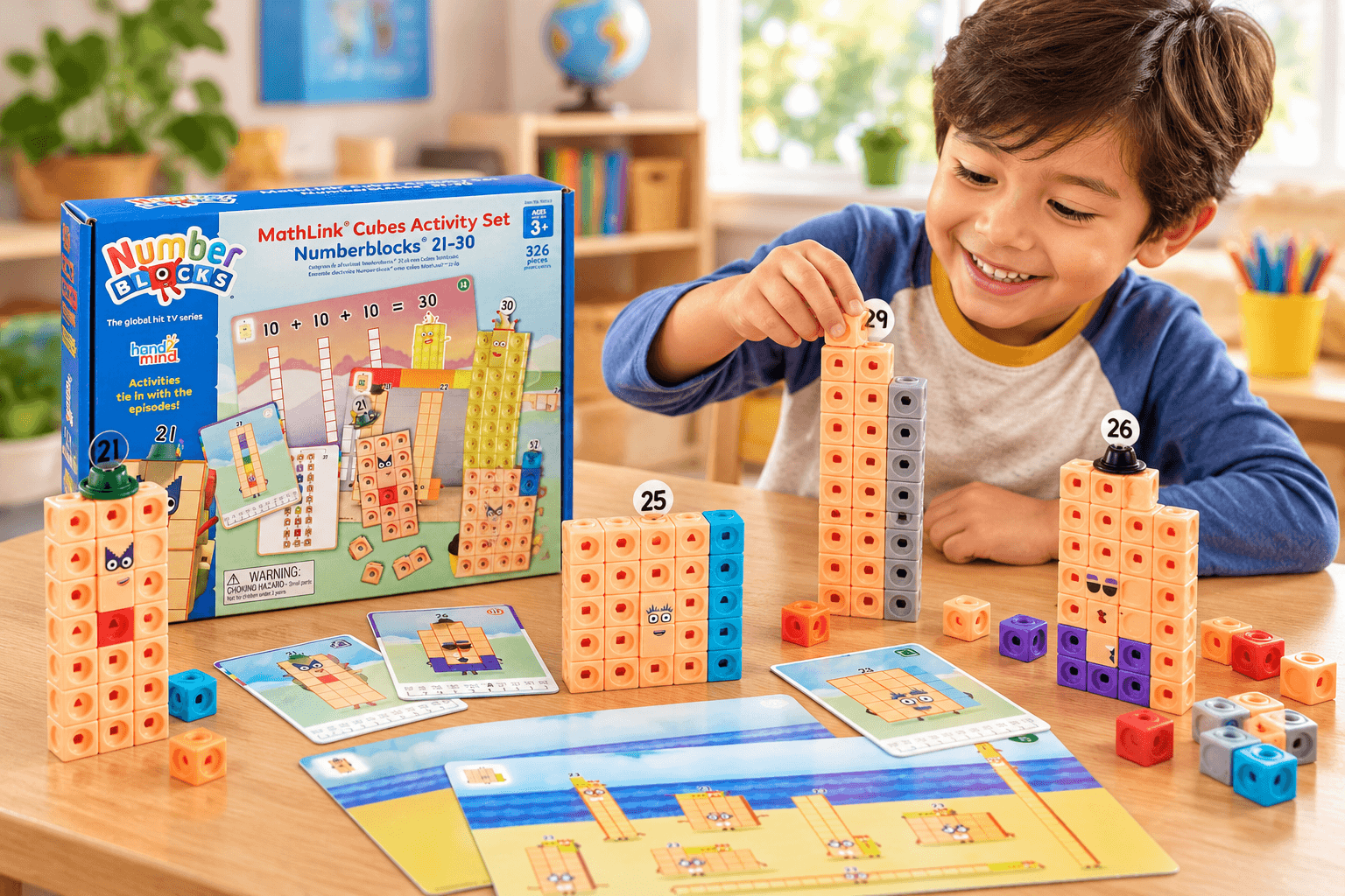 A happy boy builds Numberblocks characters using the MathLink Cubes Activity Set 21–30 in a sunny playroom. Colorful cube towers, number labels, illustrated activity cards, and the blue product box fill the wooden table.
