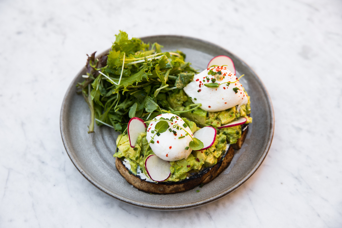 Two slices of avocado toast with poached eggs served with a green salad