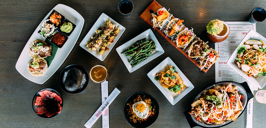 A table with an assortment of dishes including nachos, tacos, a hot stone, chop sticks, some beers