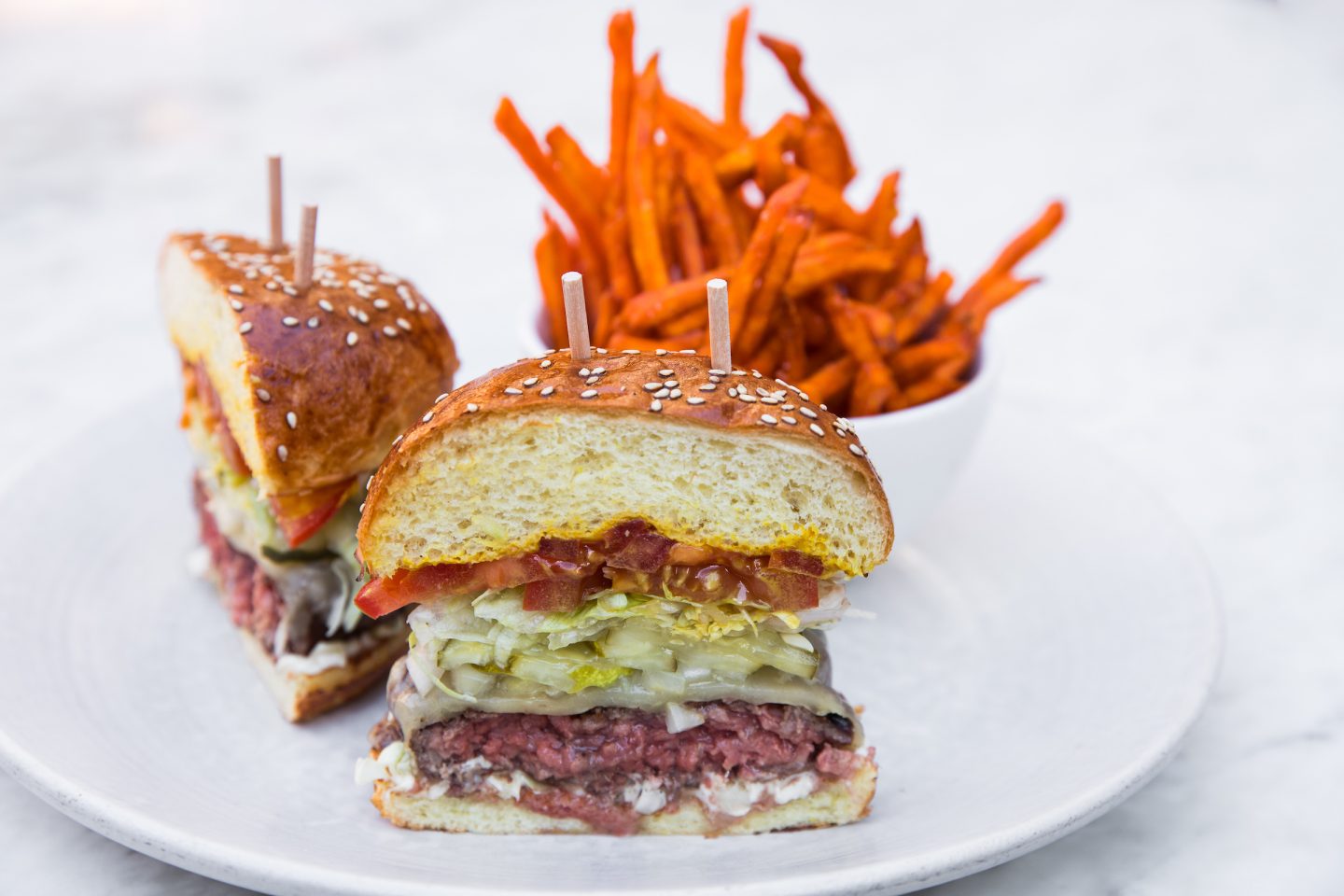 Impossible Burger cut in half with sweet potato fries.