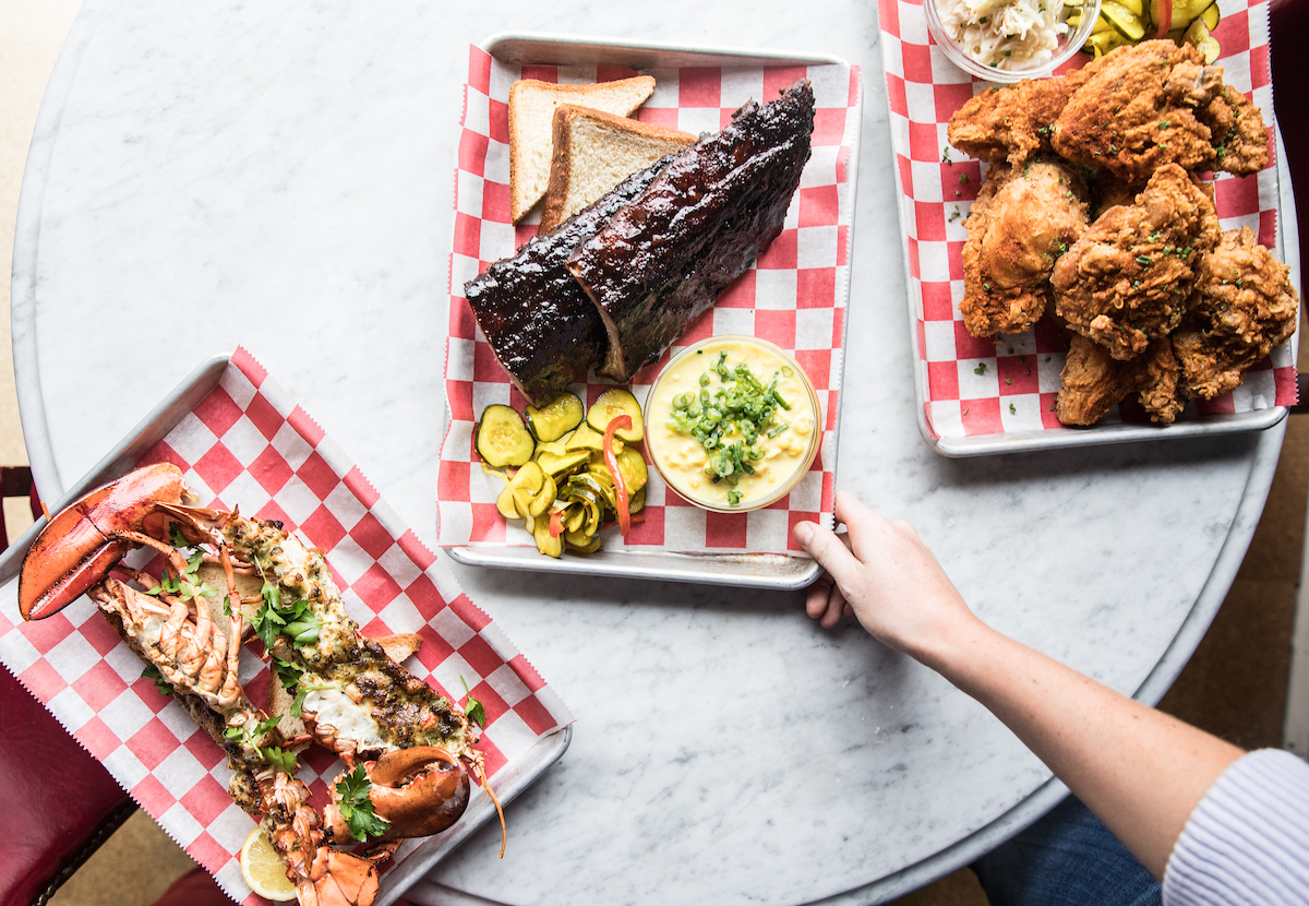 Three treys one with grilled lobster one with ribs and a side of pickles and one with fried chicken.
