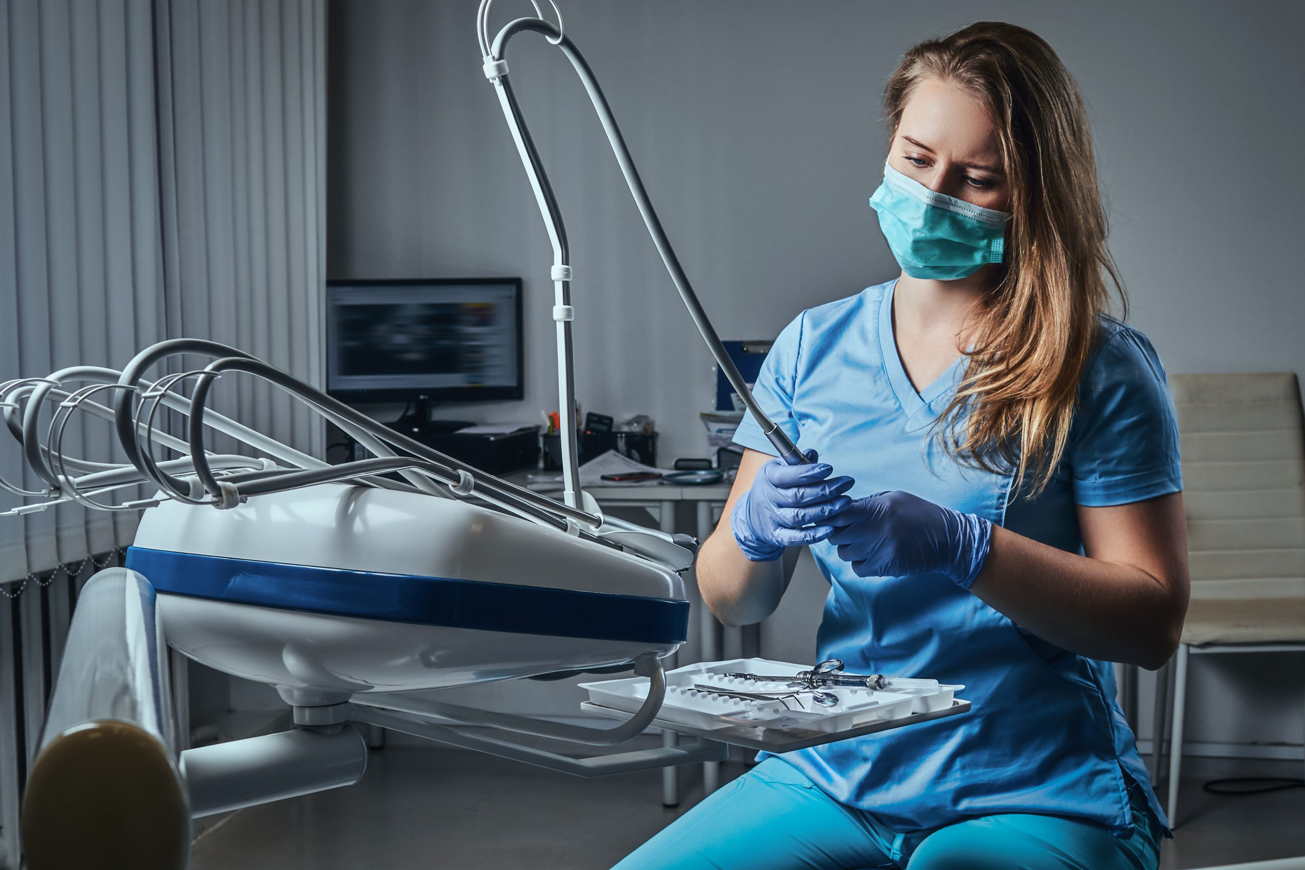 Female dentist wearing a uniform and mask sitting on a chair at his workplace in a dental clinic.