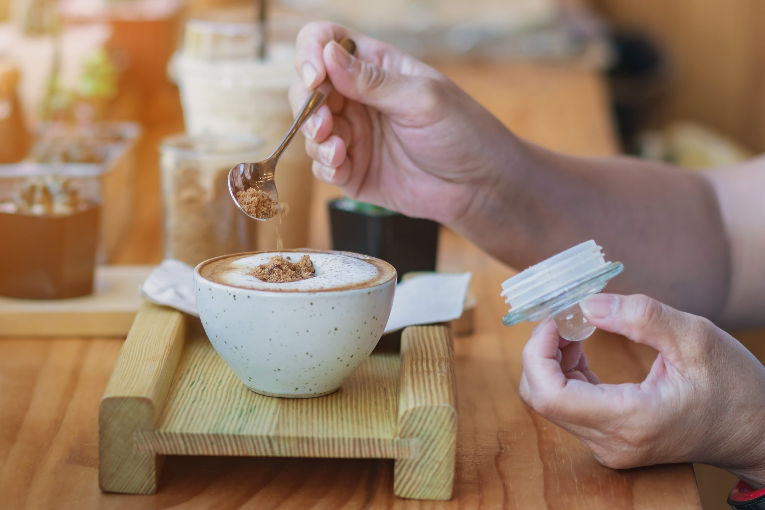 Woman pouring sugar into a white cup of coffee