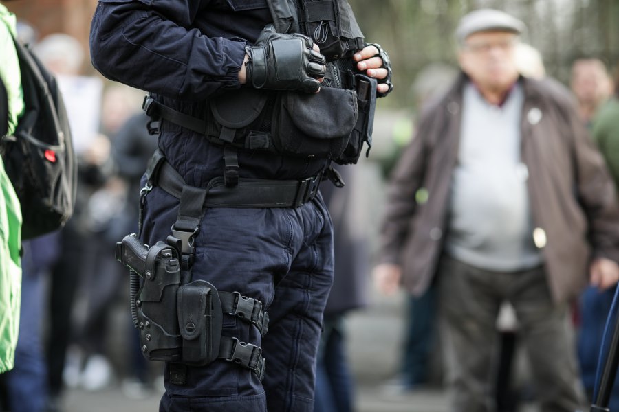 Details of the security kit of a riot police officer (including handcuffs, 9mm handgun, radio station and baton) sitting amongst civilians