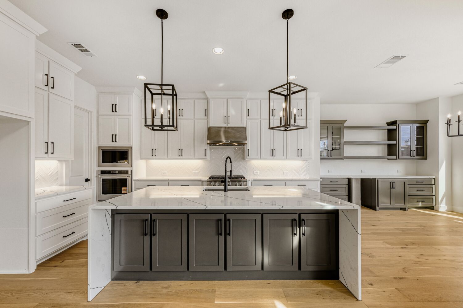 Interior of kitchen with modern pendant light fixtures above large waterfall island, including butler's pantry