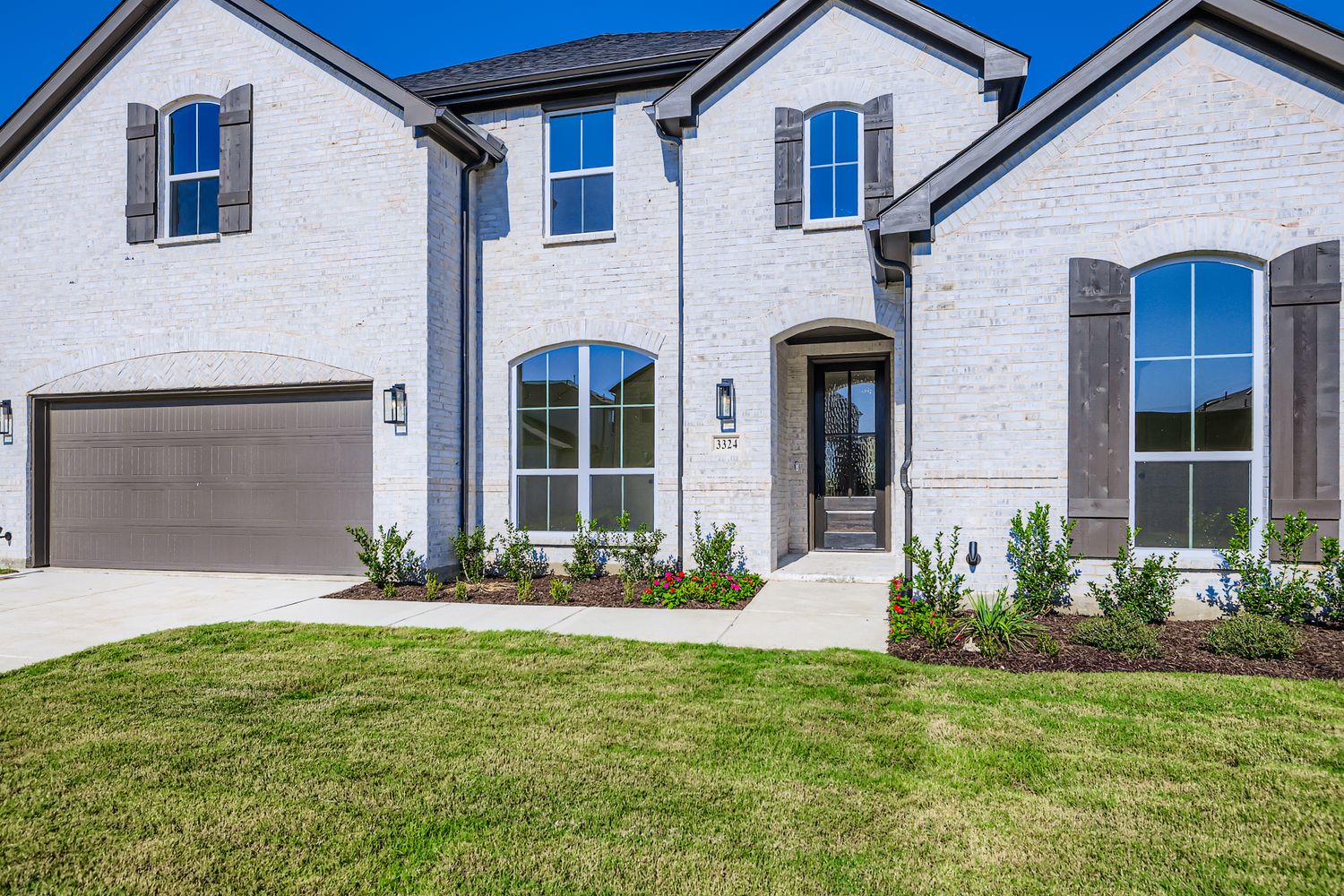 front image of two-story home, landscaped with shrubs and greenery, garage located at front