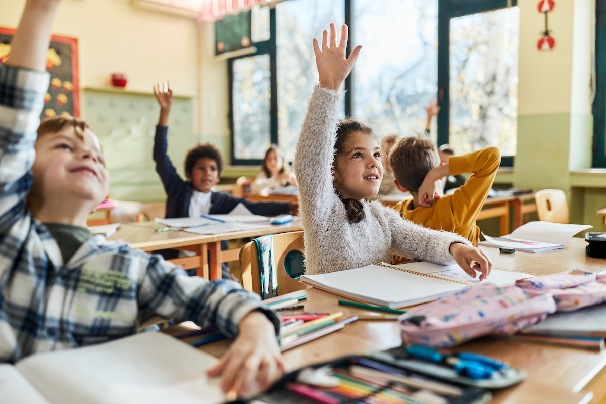 Elementary school students raising their hand in classroom.