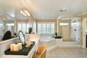 luxury bathroom with spa tub on pedestal, large shower with glass enclosure, vanity with candles, mirror and gold upholstered vanity chair