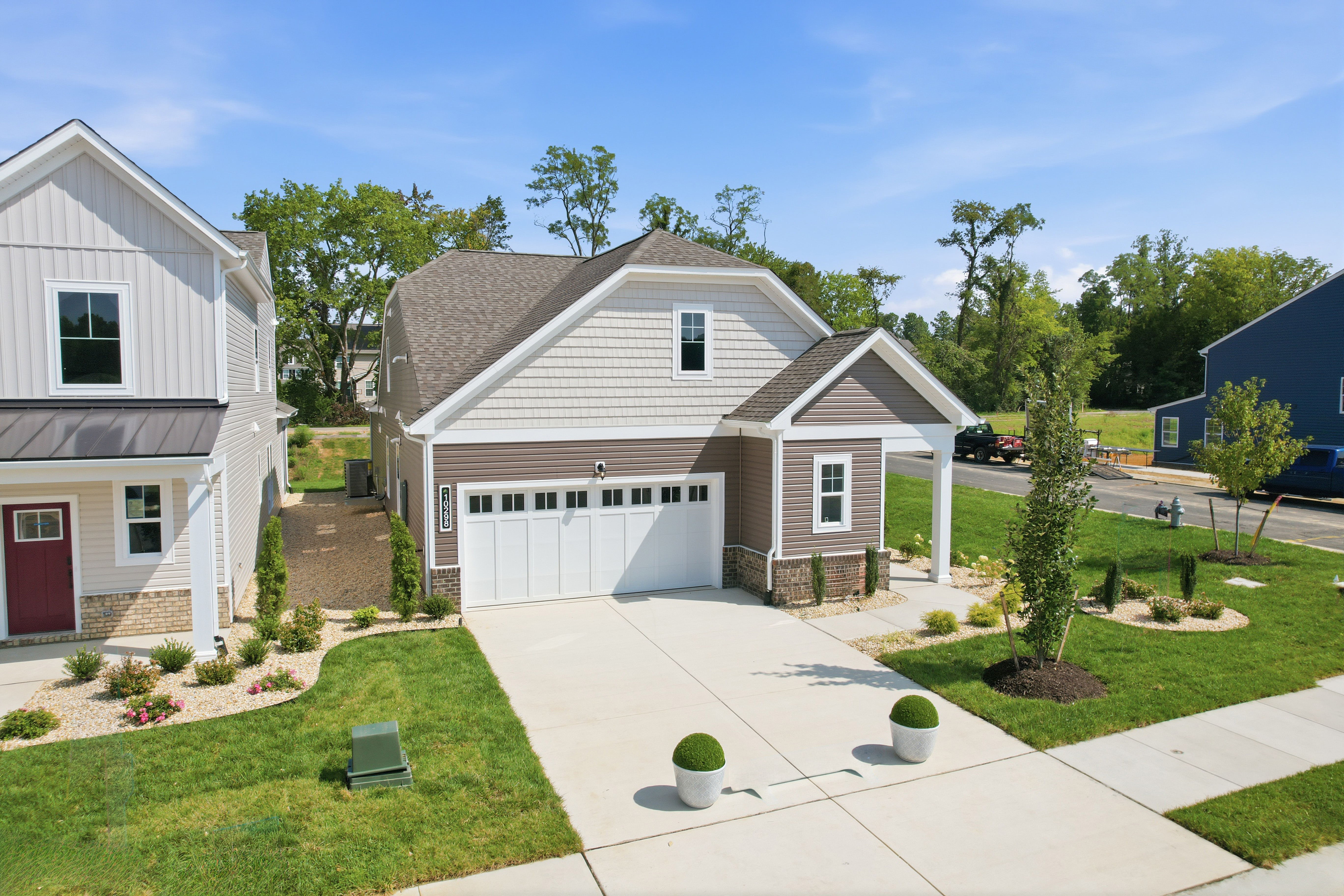 A home in the Hickory Grove neighborhood of the StyleCraft homes community. There is a garage and a paved driveway. There's a house next door, a green yard with various plants, a blue sky and trees in the background.