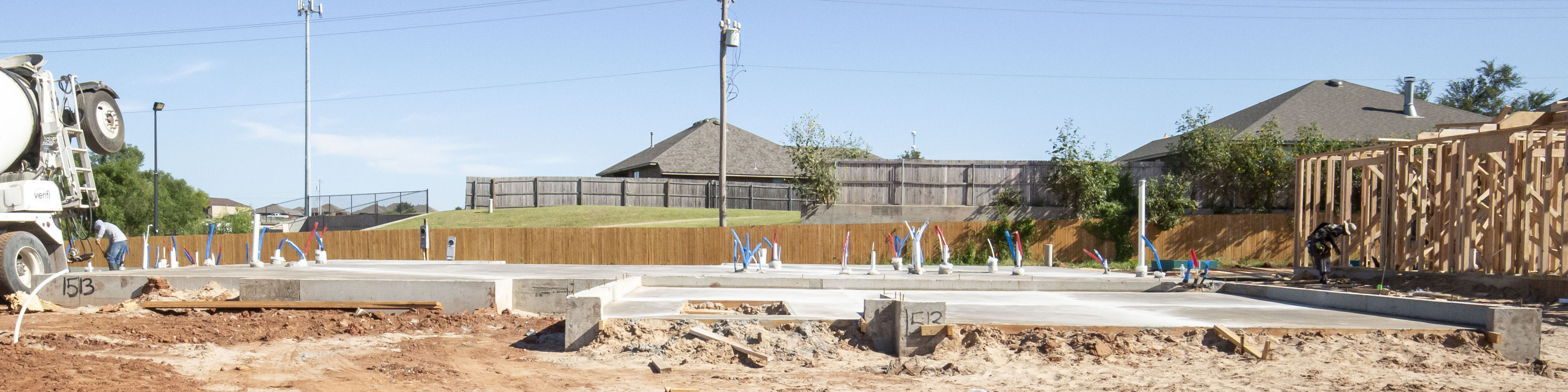 A foundation on a plot of land with a concrete truck on the left and the frame of a home on the right.