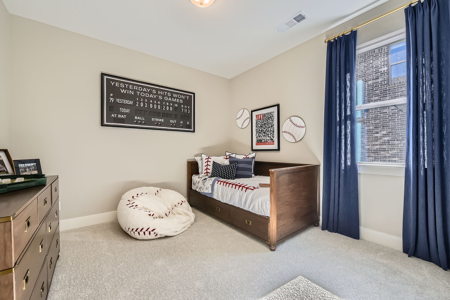 Baseball themed kid's bedroom with a trundle bed in corner and dresser.