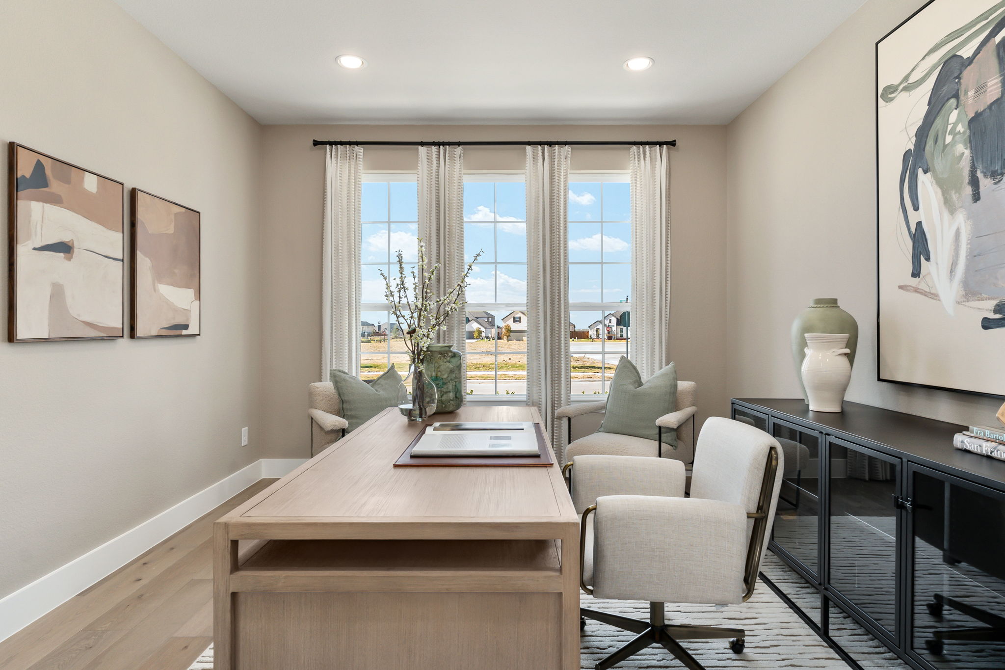 Bright and airy study, with centralized desk, cool wood tones, and three windows line the back wall