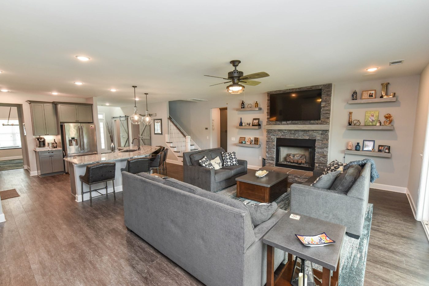 Great room with TV wall, fireplace, ceiling fan, and open kitchen layout in an Ernest Homes model