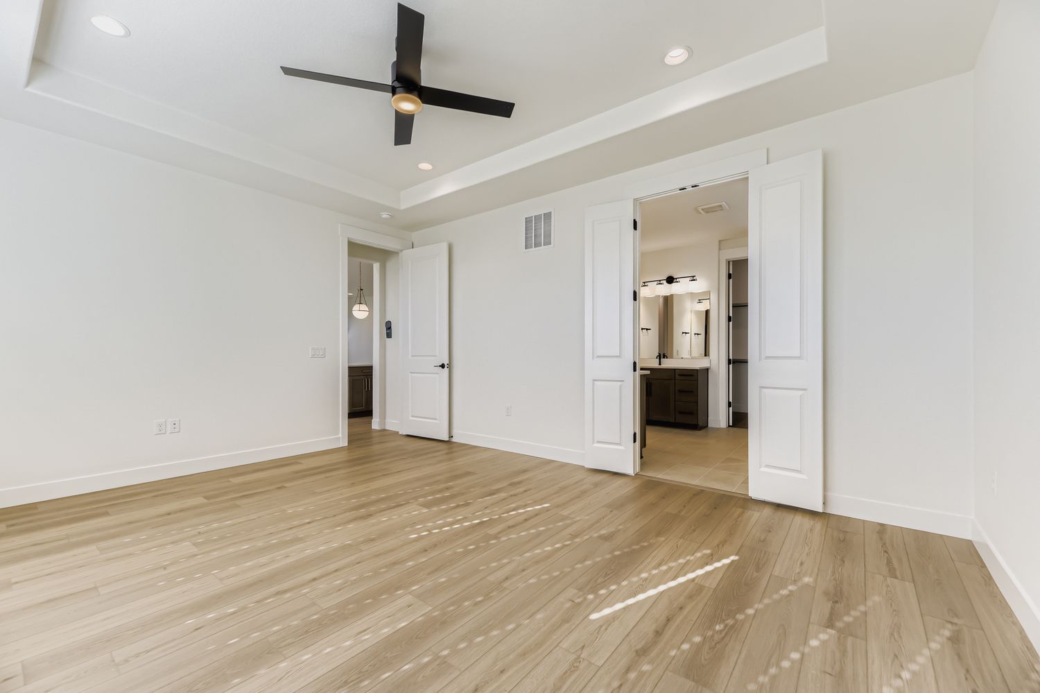 Main bedroom suite with modern ceiling fan and double doors that open into the primary bathroom