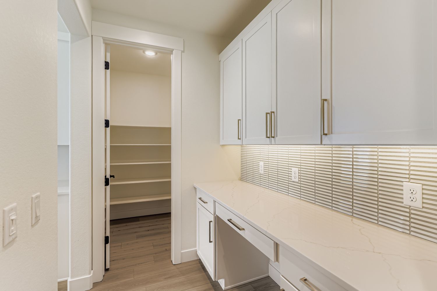 built-in desk area with cabinetry overhead and hallway that leads to expansive pantry