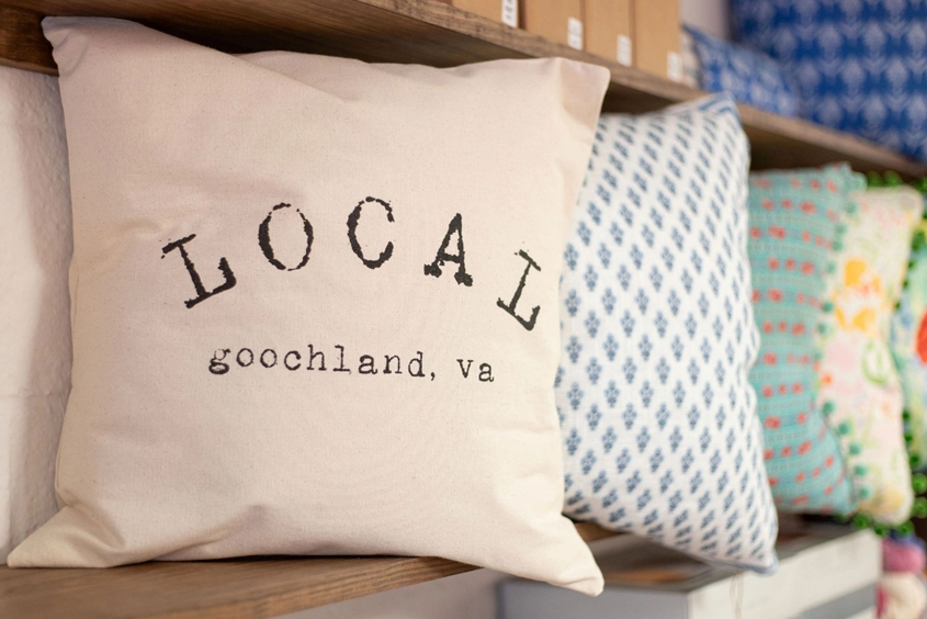 Cream-colored pillow with the words "Local Goochland, VA" on a store shelf