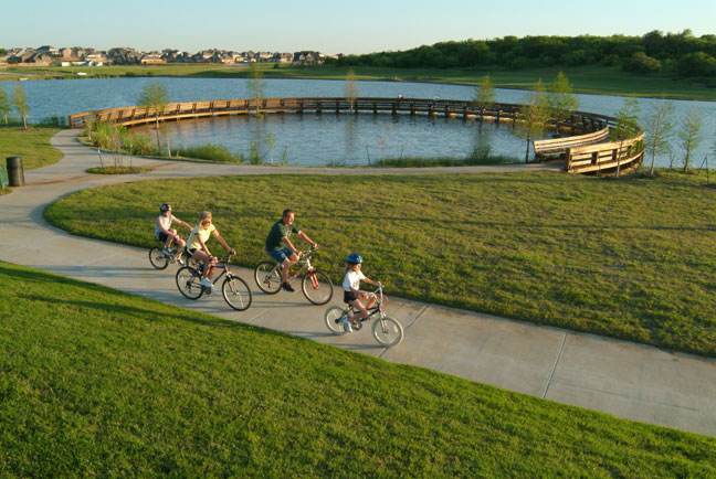 family biking together in the neighborhood next to large scenic lake