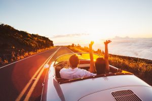 couple in convertible driving along highway near ocean