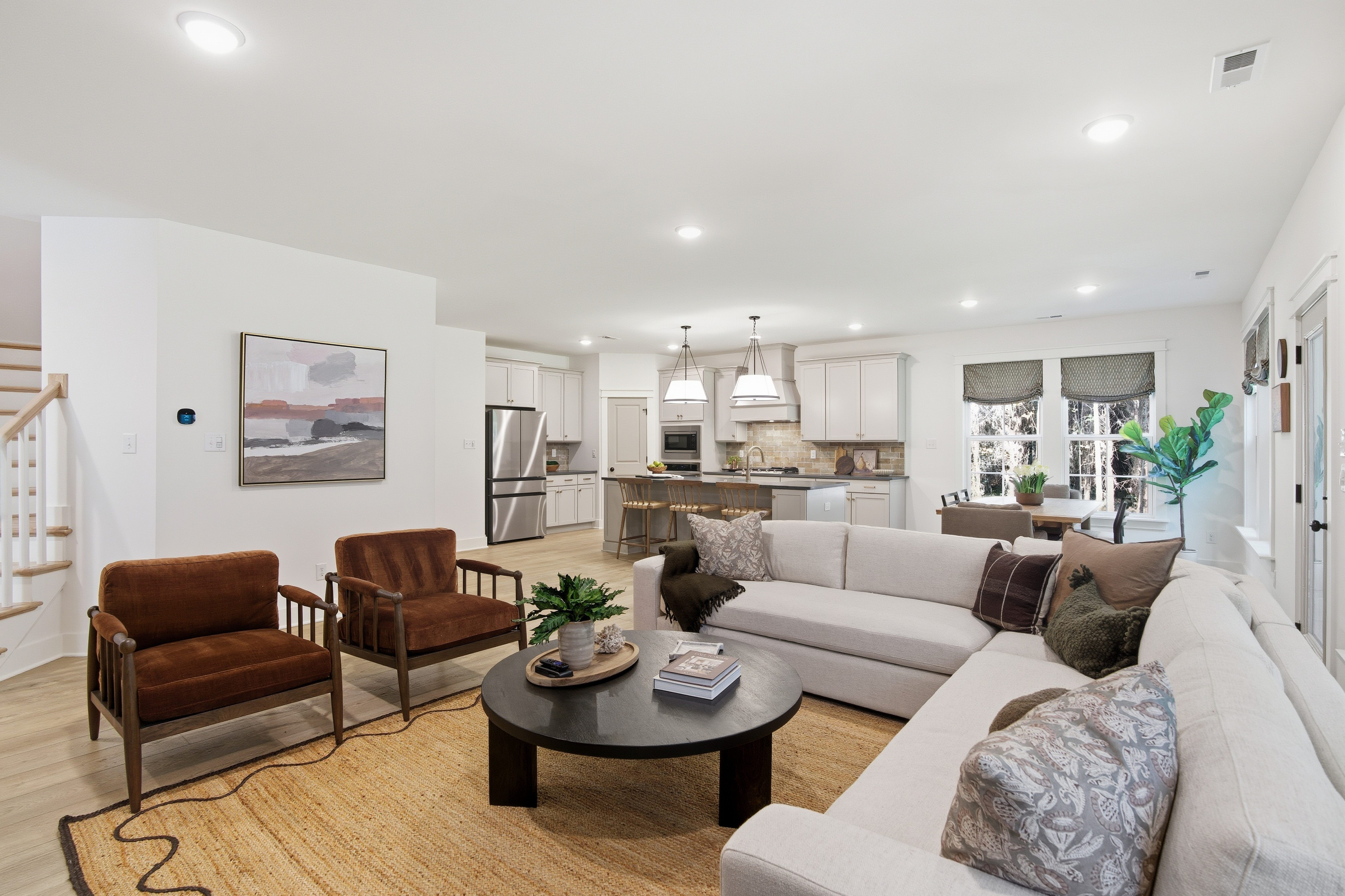 The living from from the Appomattox plan from StyleCraft Homes. There's a couch, chairs, coffee table, art on the white walls, and stairs and a kitchen in the background.