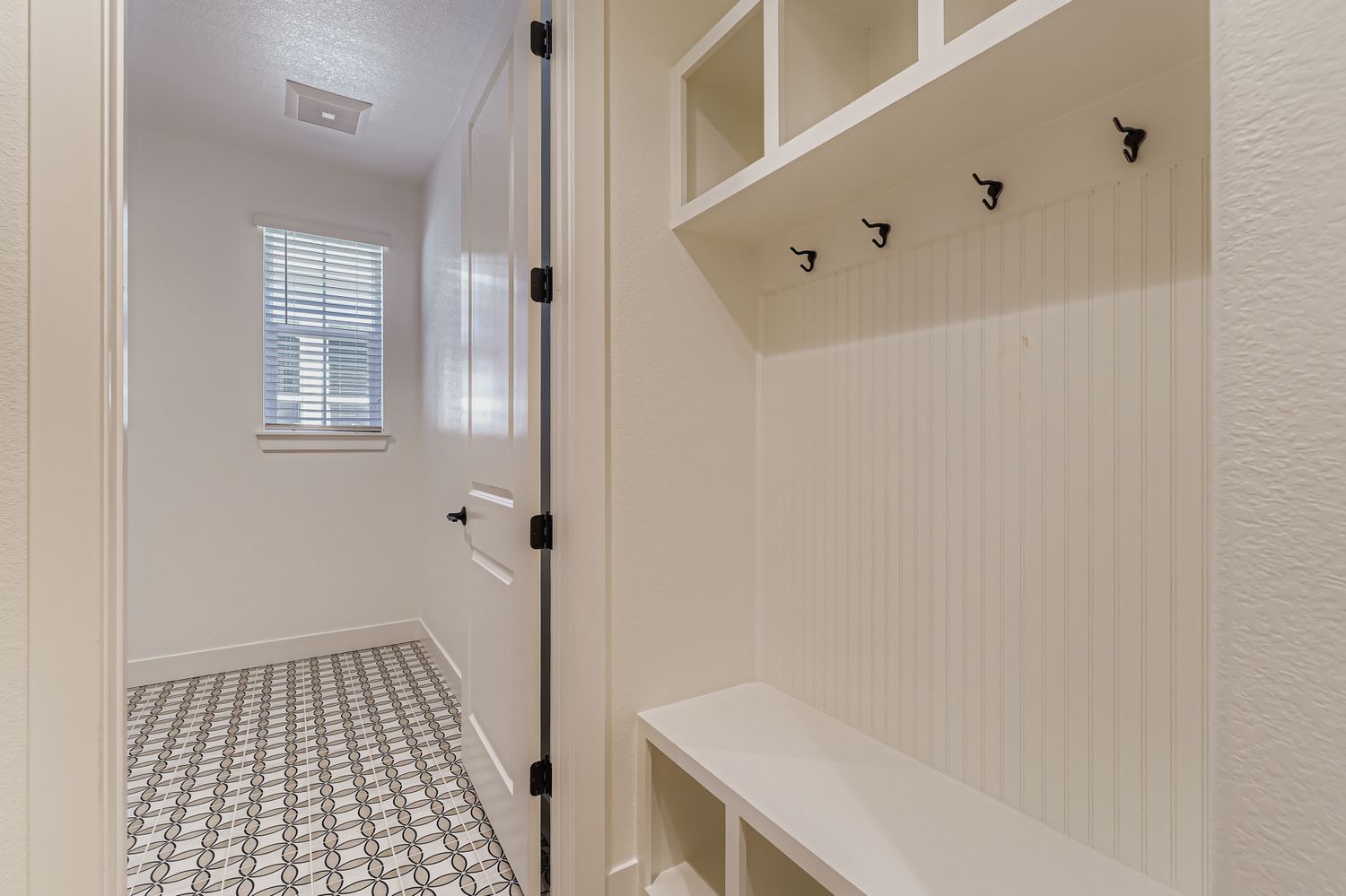 Mudroom bench with hangers and built-in cabinetry leading to the tiled laundry room