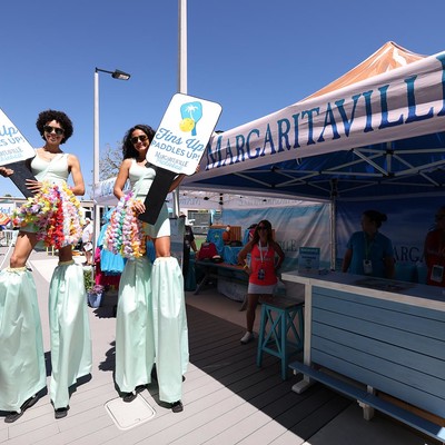 Two women on stilts holding Fins Up Paddles Up! signs