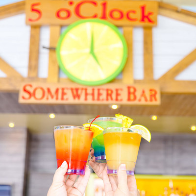 People doing cheers with three colorful drinks in front of 5 o'Clock somewhere Bar-