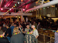 Group handing under red and green string lights, drinks in hand and leis around their necks