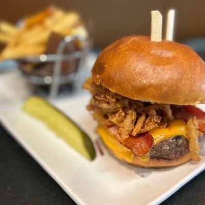 Photo of gourmet cheeseburger with crispy onion straws, served with french fries and a pickle spear