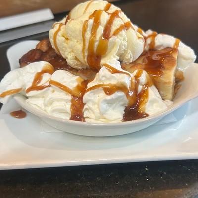 Photo of warm dessert topped with vanilla ice cream, whipped cream, and caramel drizzle