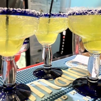 Photo of glasses of yellow frozen margaritas with blue salted rims lined up at the bar