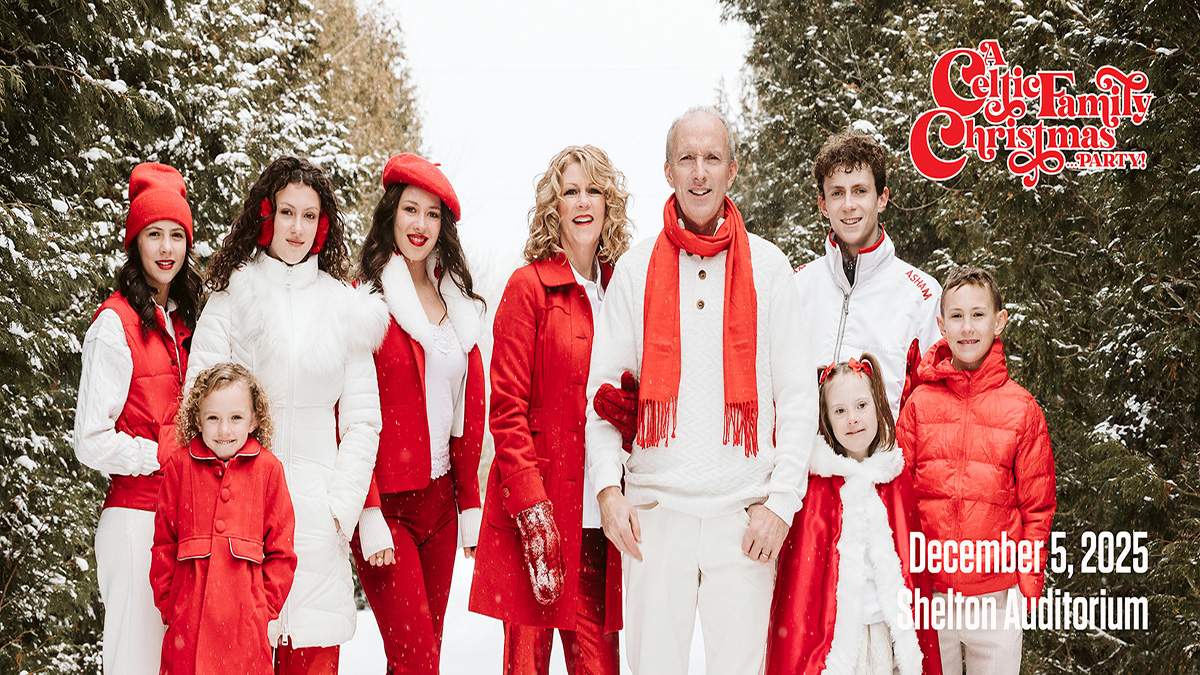 Family dressed in white and red winter gear outside in the snow among Christmas trees