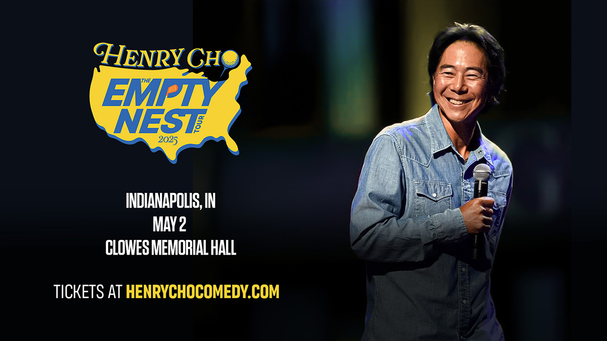 Henry Cho holding a microphone on stage