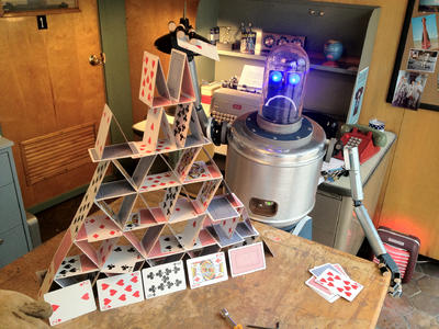 playing cards stacked in a pyramid with a robot behind it with a sad face