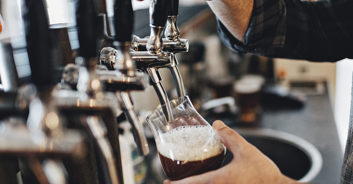 Male hand pulling down on beer tap and pouring a dark beer into glass.