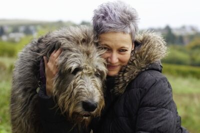 Irish Wolfhound being hugged by a middle-aged woman outdoors.