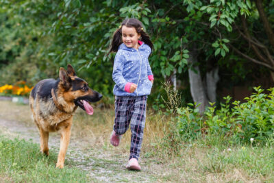 young girl running outdoors with a german shepherd dog