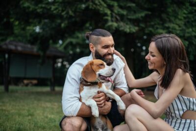 Beagle being hugged by a man and woman in the yard. people