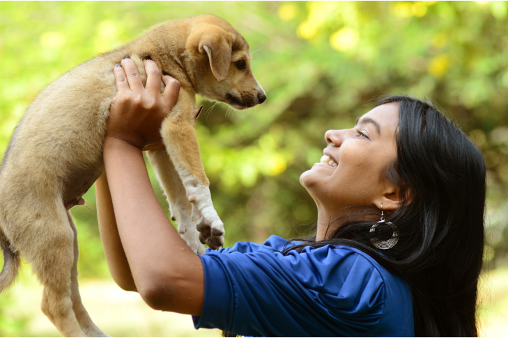 Mixed breed puppy being held up by a teenage girl outdoors.