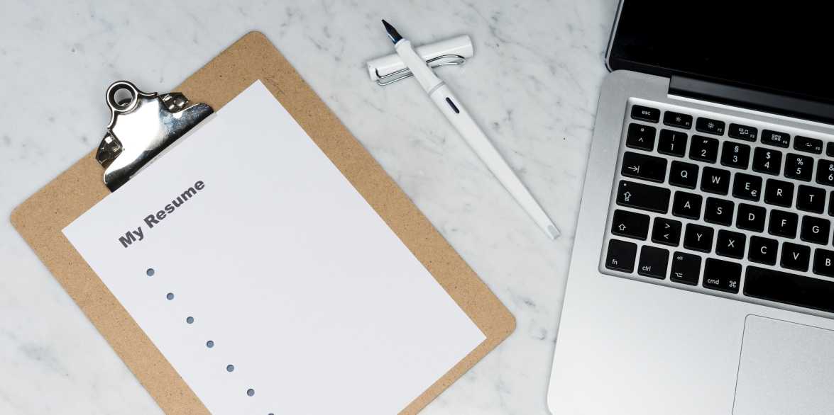 A laptop computer, pen, and clipboard with a piece of paper that reads, My Resume, with a column of bullet points