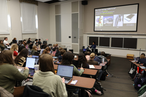 Students in a geology class lecture, sitting in a classroom with stadium style seating and listening to the professor in the background