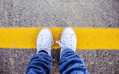 Person wearing white Converse sneakers, standing on a yellow line in the road