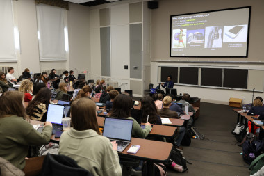 Students in a geology class lecture, sitting in a classroom with stadium style seating and listening to the professor in the background