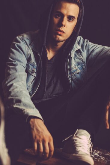 Domina el Arte del Layering Casual. Joven con estilo urbano vistiendo una chamarra de mezclilla sobre una sudadera con capucha, un ejemplo de look casual moderno para hombre.