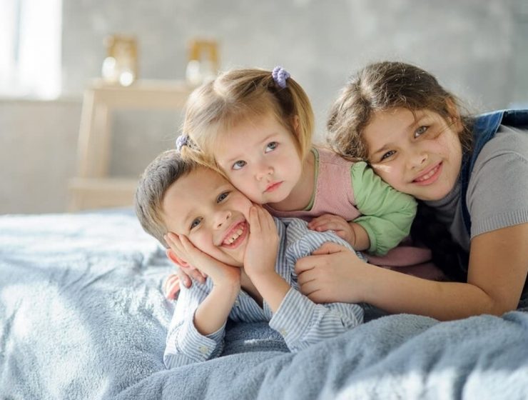 Hermano mayor, menor o del medio: cómo sos según el orden en que naciste 10 Fotografía de tres niños abrazados sobre una cama, reflejando la ternura, cercanía y complicidad entre hermanos.