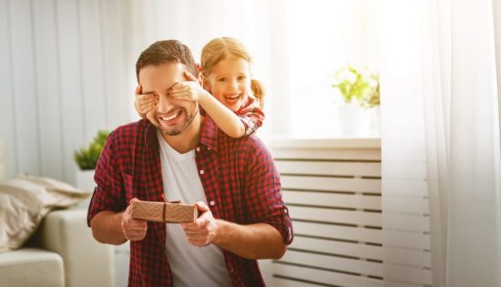 Niña feliz tapando los ojos de su padre para darle una sorpresa y un regalo por el Día del Padre.