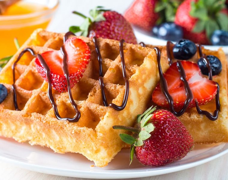 Waffles caseros dorados con fresas y arándanos frescos, decorados con chocolate derretido. Una receta deliciosa y fácil para un desayuno perfecto o brunch irresistible.