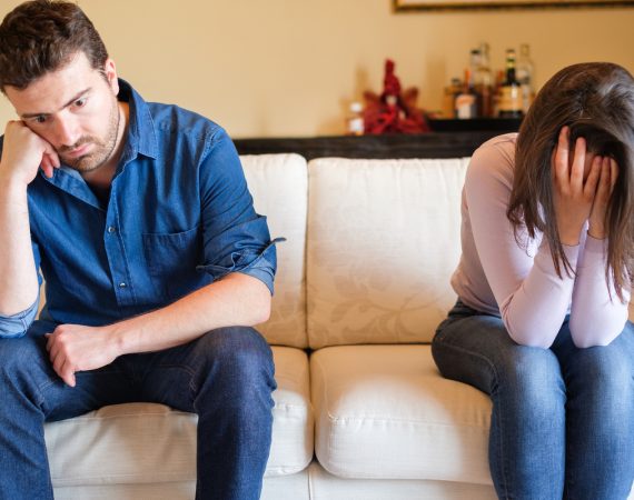 Pareja con problemas sentimentales sentada en un sofá, mostrando tristeza y distanciamiento.